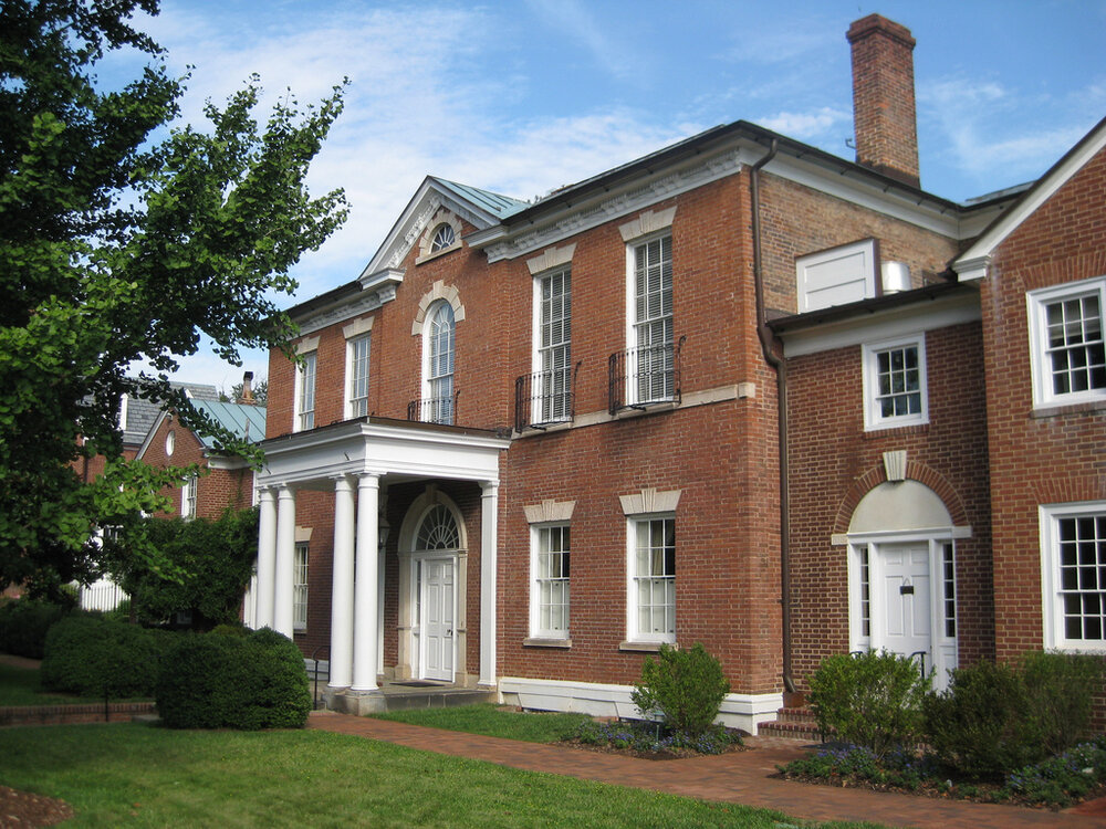 A brick house with white panels in the front and a tree slightly obscuring the view
